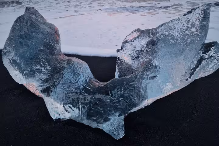 Translucent glacial ice chunk on black sand beach with ocean waves in Iceland