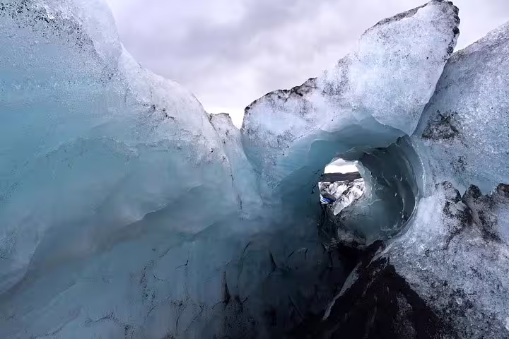 Ice cave tunnel through glacial formations on Iceland's south coast with overcast sky