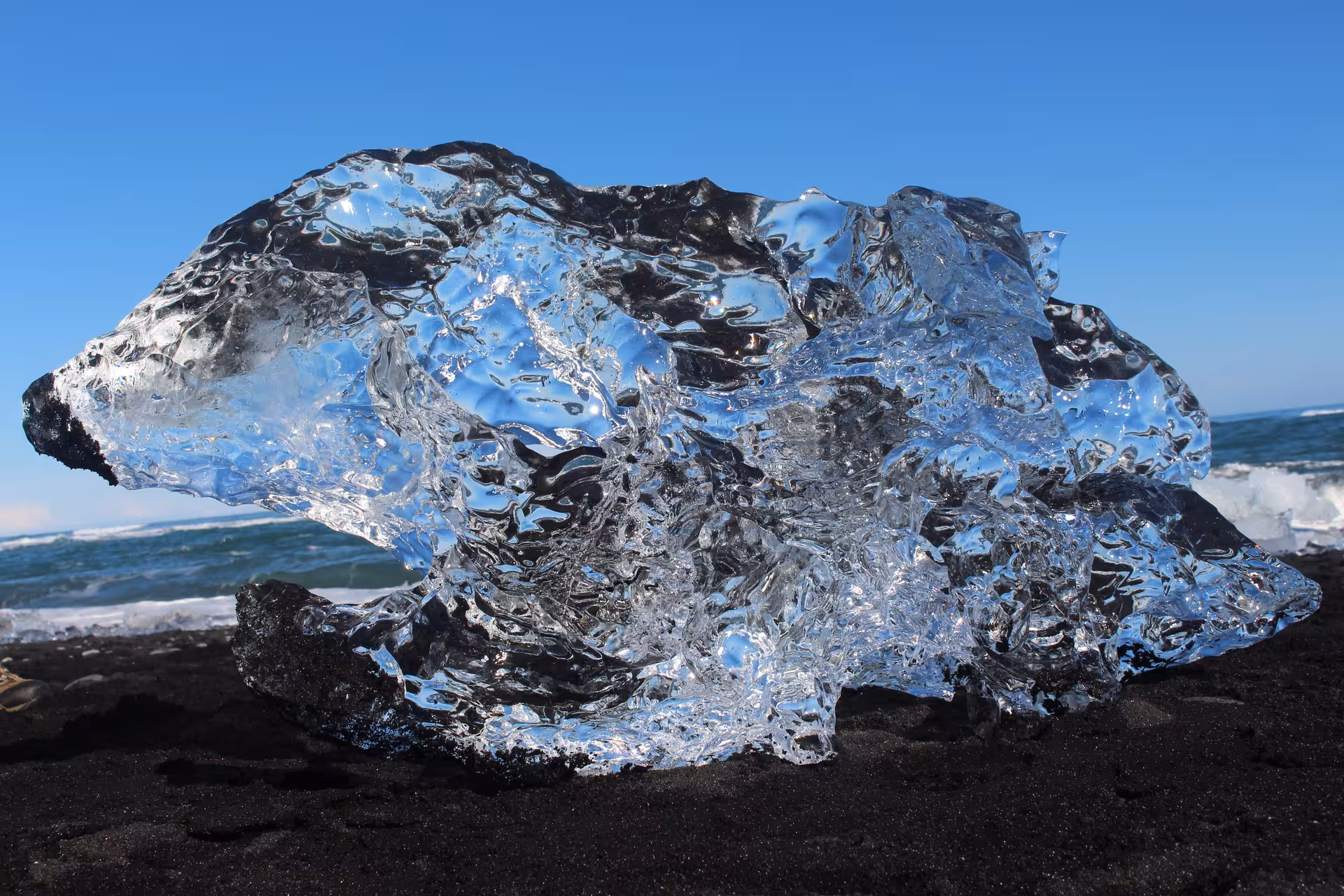 Crystal clear glacial ice chunk resting on black sand beach at Jokulsarlon with ocean waves in background