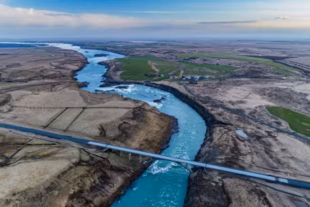 Aerial view of a turquoise glacial river winding through Iceland's volcanic landscape with a bridge crossing