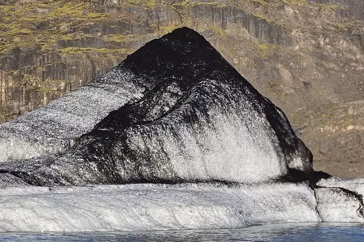 Dark ash-covered glacier ice formation with cascading meltwater on Iceland's south coast