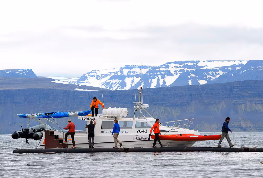Support boat with sea kayaks and guides in a glacier fjord, preparing for Glacier Fjords Kayaking adventure
