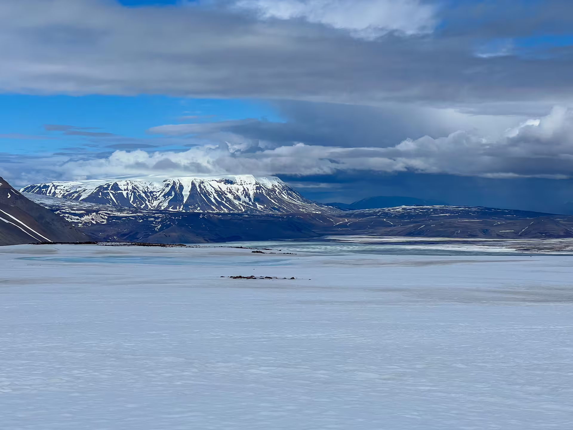 Snow-covered flat-topped mountain overlooking a frozen glacial plain under dramatic cloudy skies in Iceland