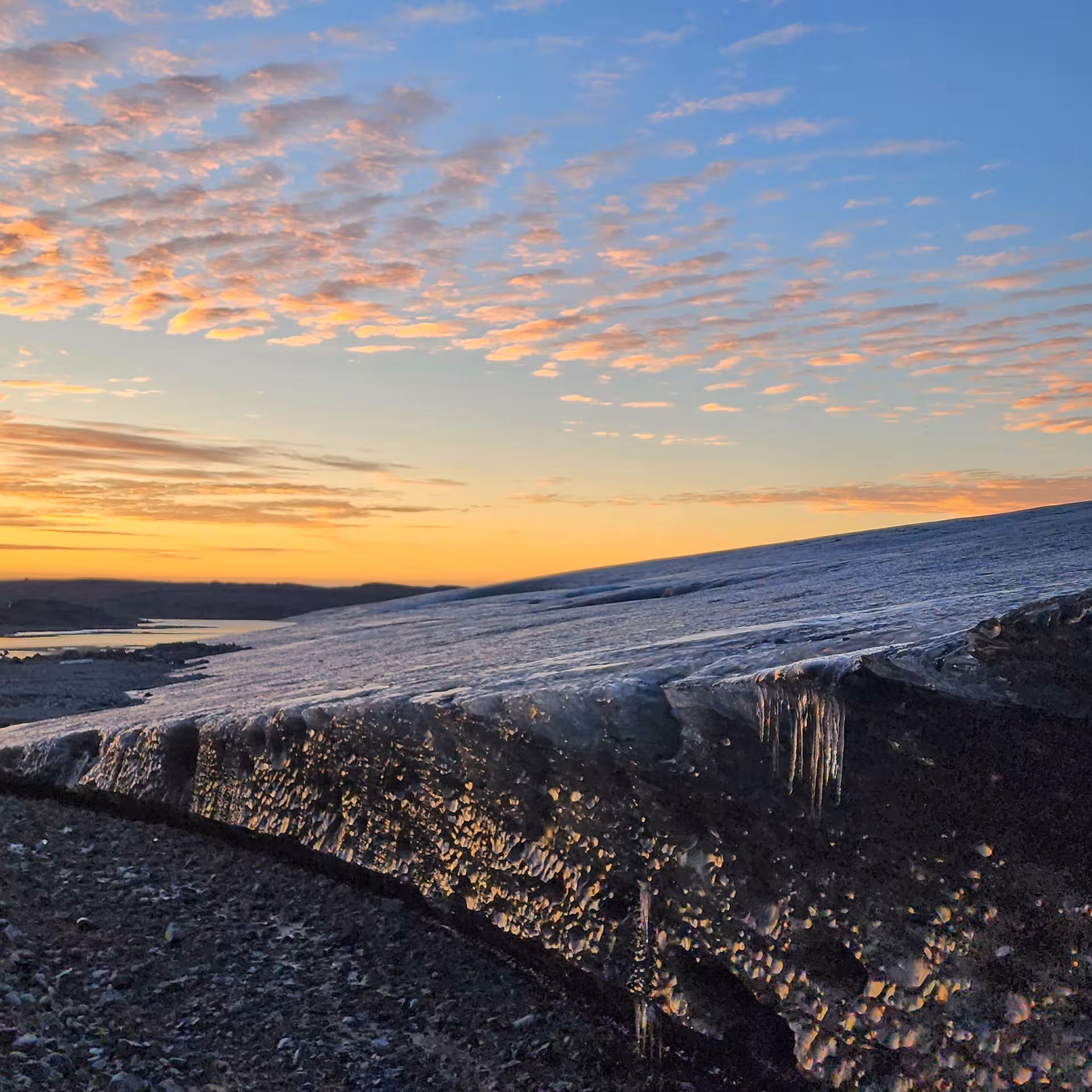 Melting glacier edge with icicles on black sand beach at golden sunset in Iceland
