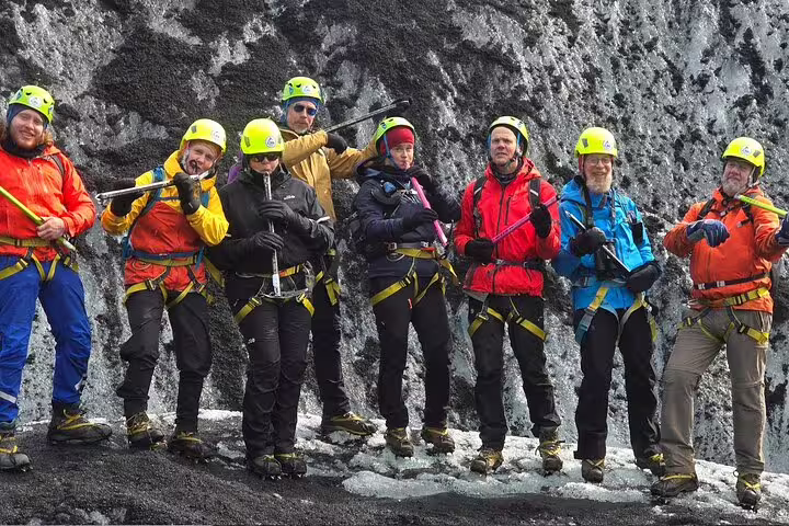 Group of eight glacier hikers in yellow helmets and crampons posing on black volcanic ice wall