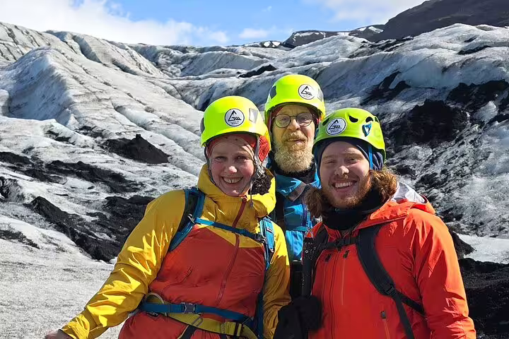 Three smiling hikers in helmets and colorful jackets posing on a glacier in Iceland