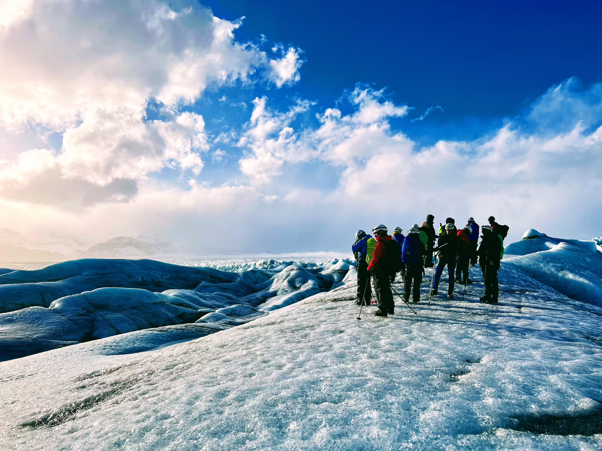 Group of hikers exploring a vast glacier landscape under a dramatic blue sky at Skaftafell, Iceland