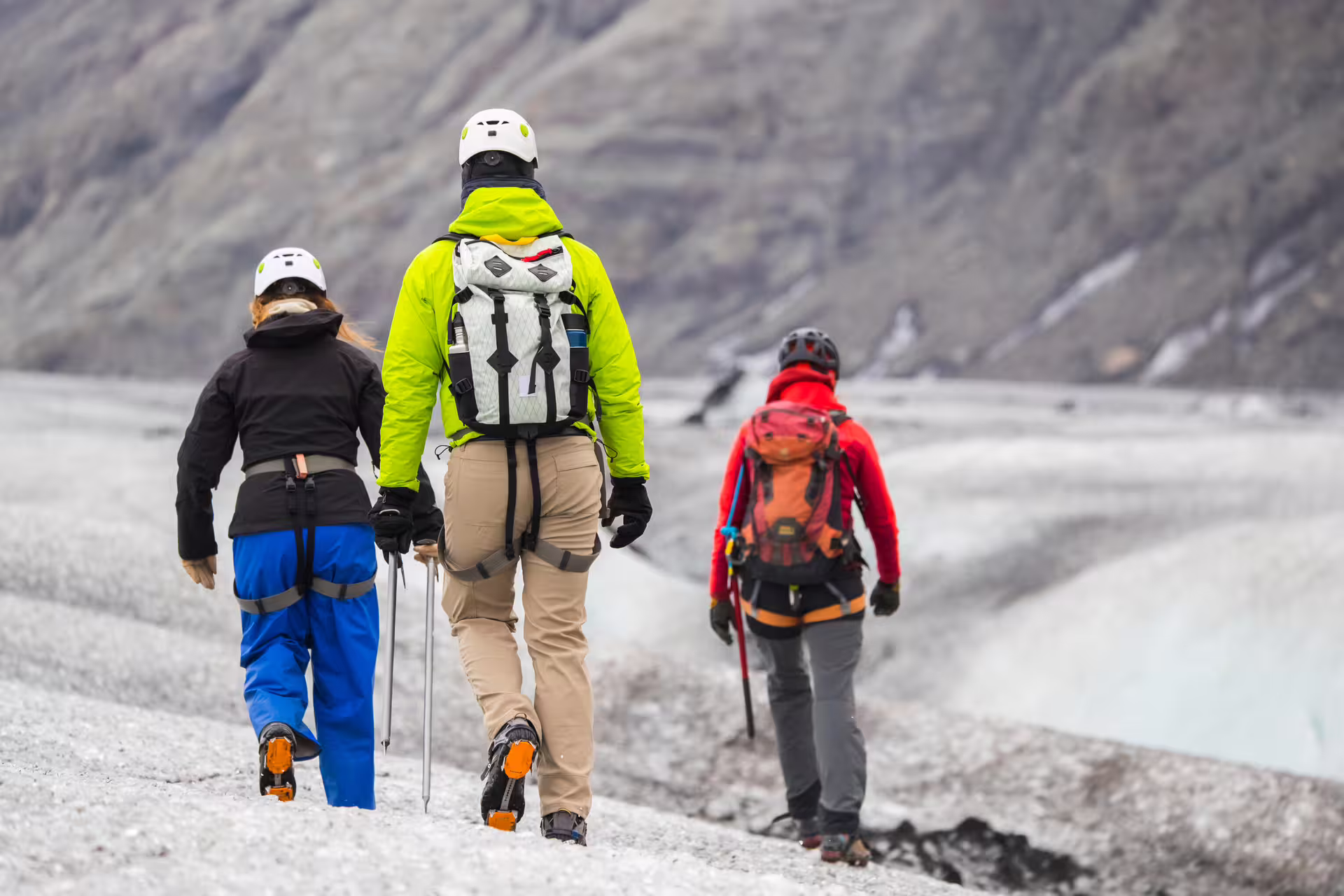 Three hikers with helmets and crampons walking across a glacier with mountain backdrop in Iceland