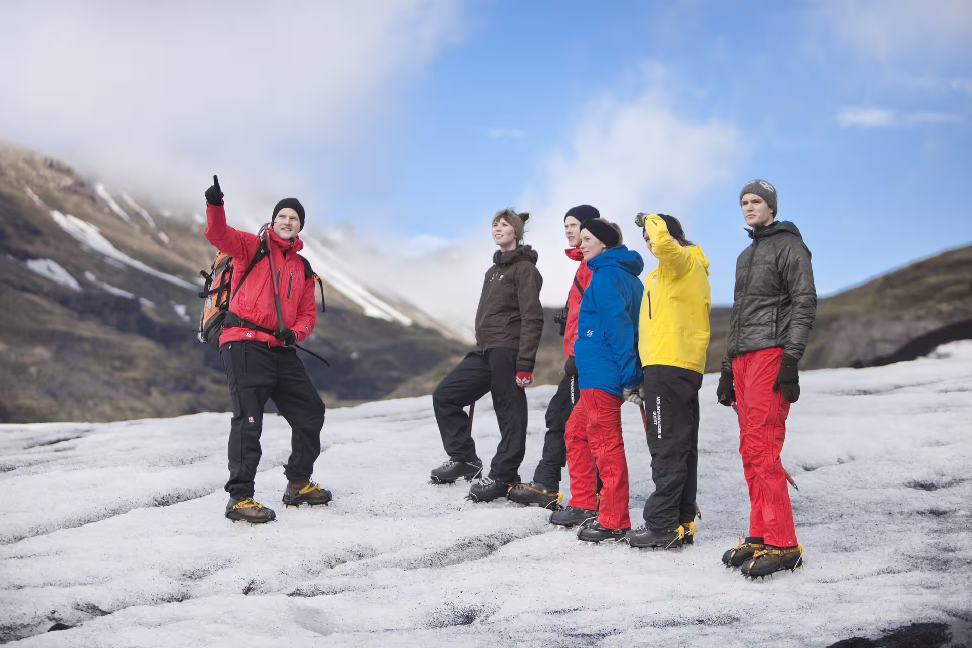 Tour guide pointing at glacier landscape with group of hikers wearing crampons on South Iceland ice field