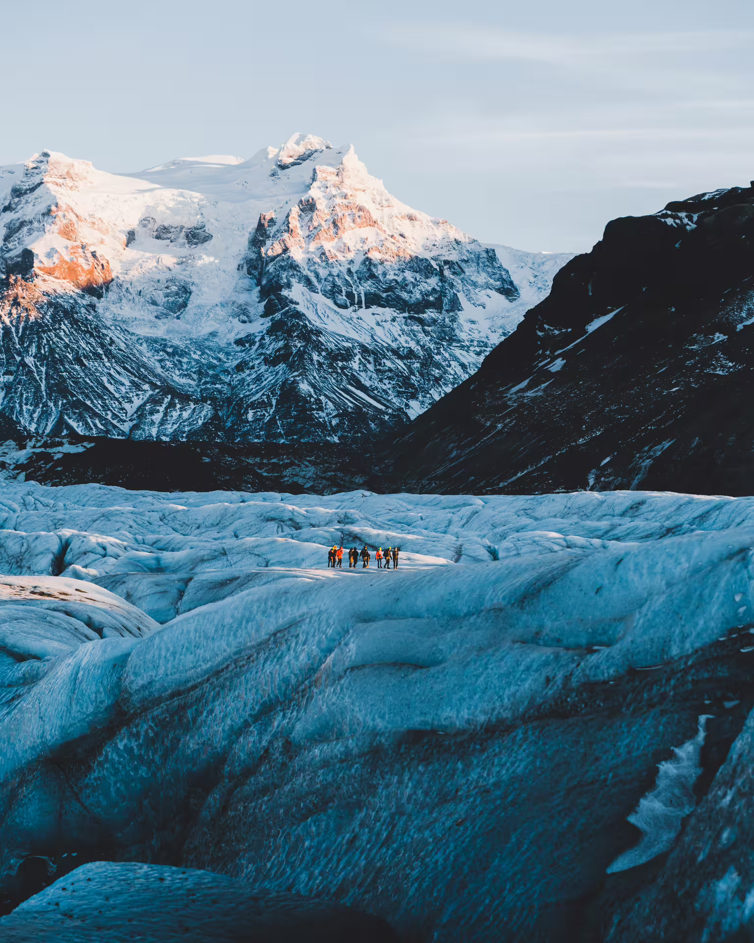 Group of hikers walking on a blue glacier with snow-capped mountains in South Iceland