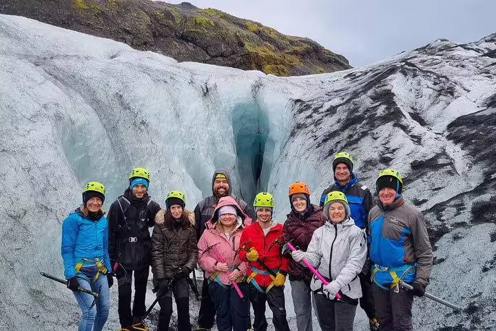 Group of tourists in helmets posing on Icelandic glacier with ice picks during guided hike
