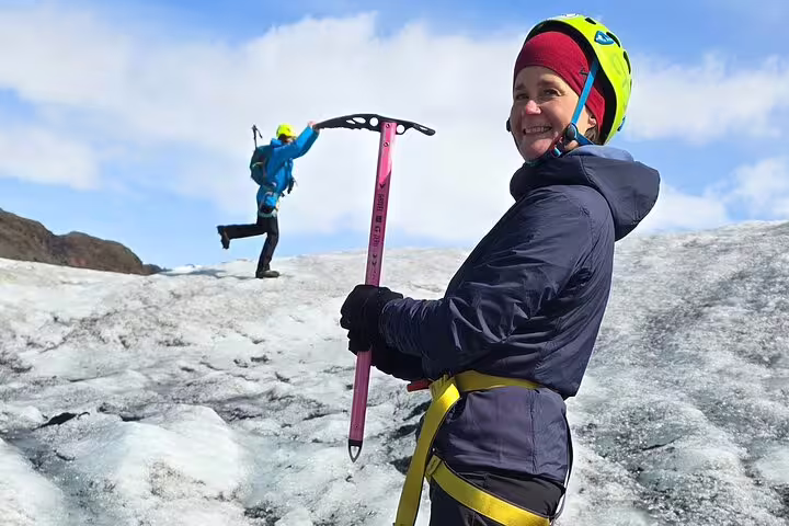 Smiling hiker holding pink ice axe on glacier with climbing partner in background, Iceland
