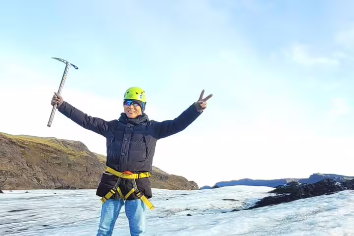 Happy hiker with ice axe and safety harness celebrating on glacier in Iceland