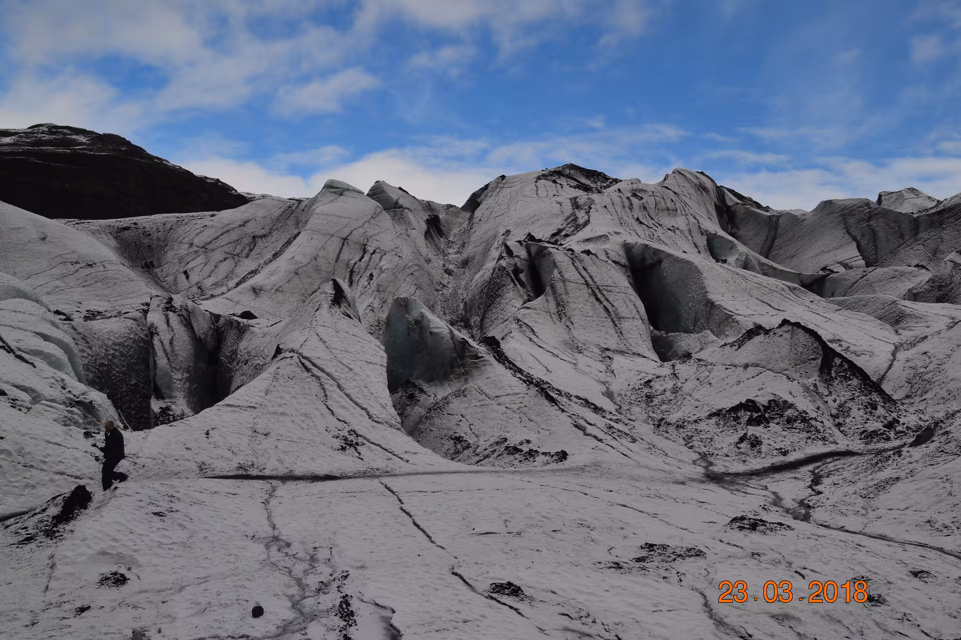 Hiker standing on ash-streaked glacier ice formations during a guided glacier hike in Iceland