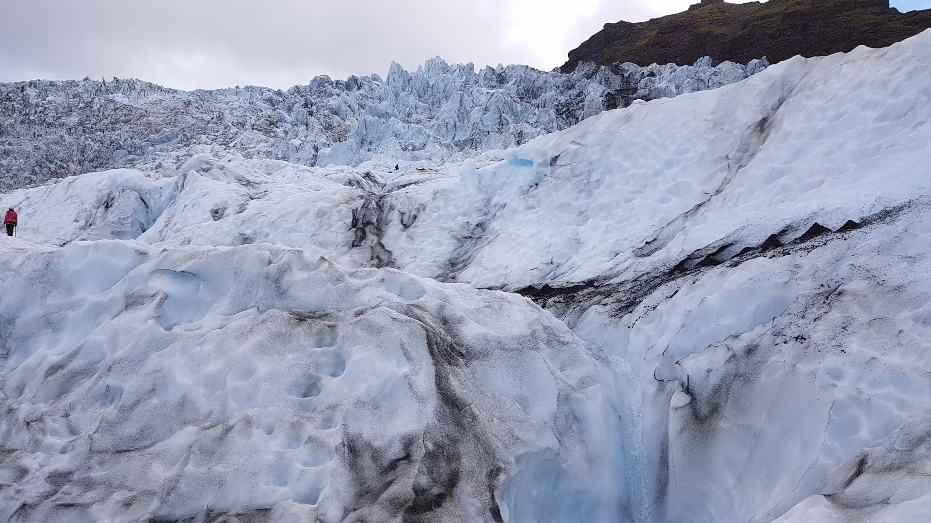Hiker in red jacket on rugged glacial ice formations during a guided glacier hike in Iceland