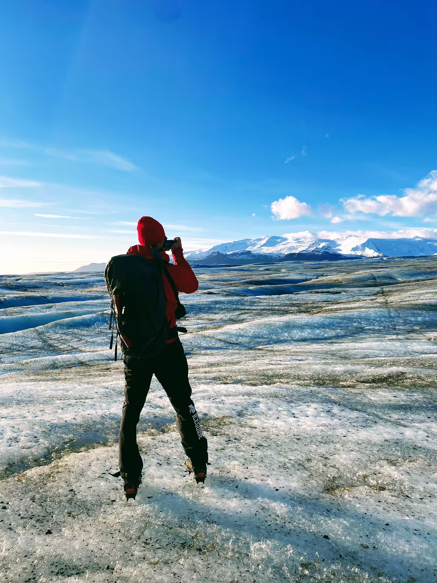 Hiker in red jacket photographing glacier landscape with snow-capped mountains at Skaftafell, Iceland