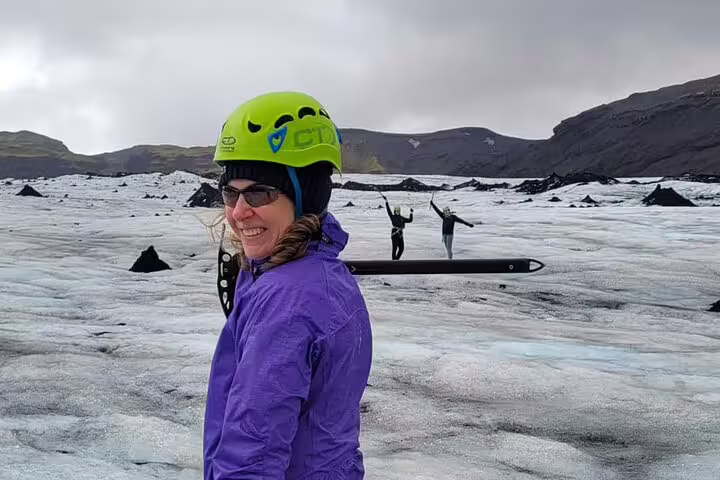 Smiling woman in green helmet on Icelandic glacier with two hikers posing in background