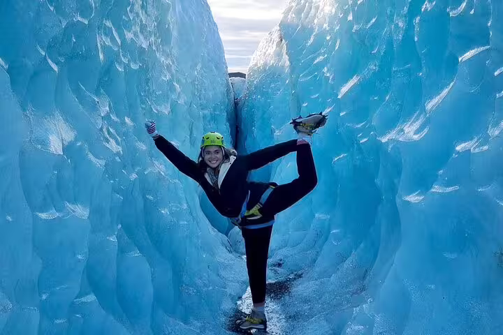 Smiling hiker in green helmet doing yoga pose between blue glacier ice walls
