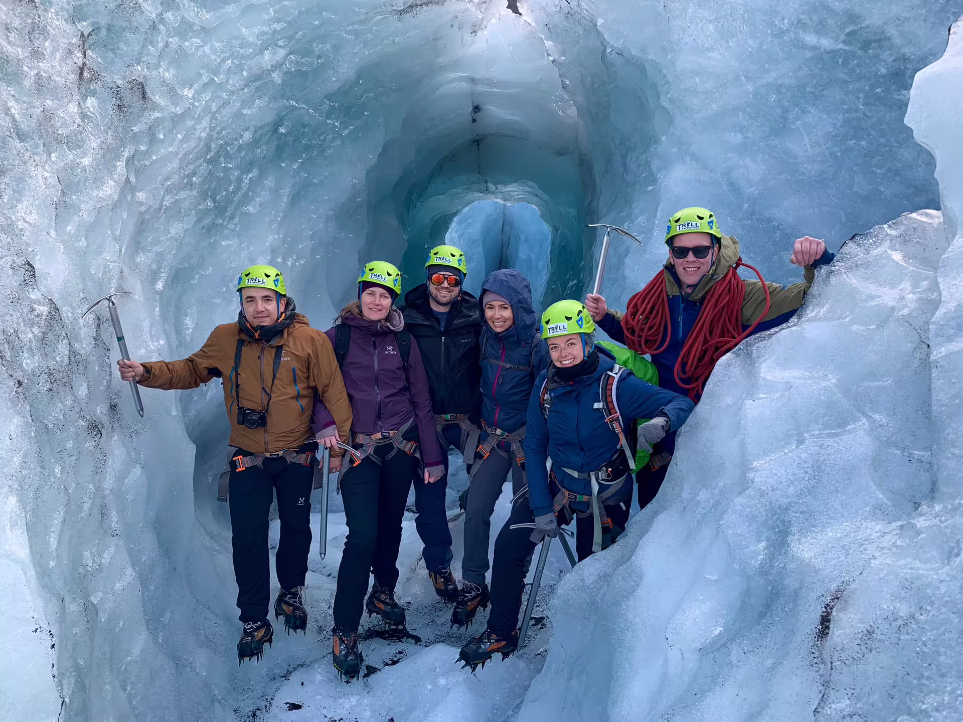 Group of hikers with ice axes and crampons posing inside a glacial ice cave tunnel in Iceland
