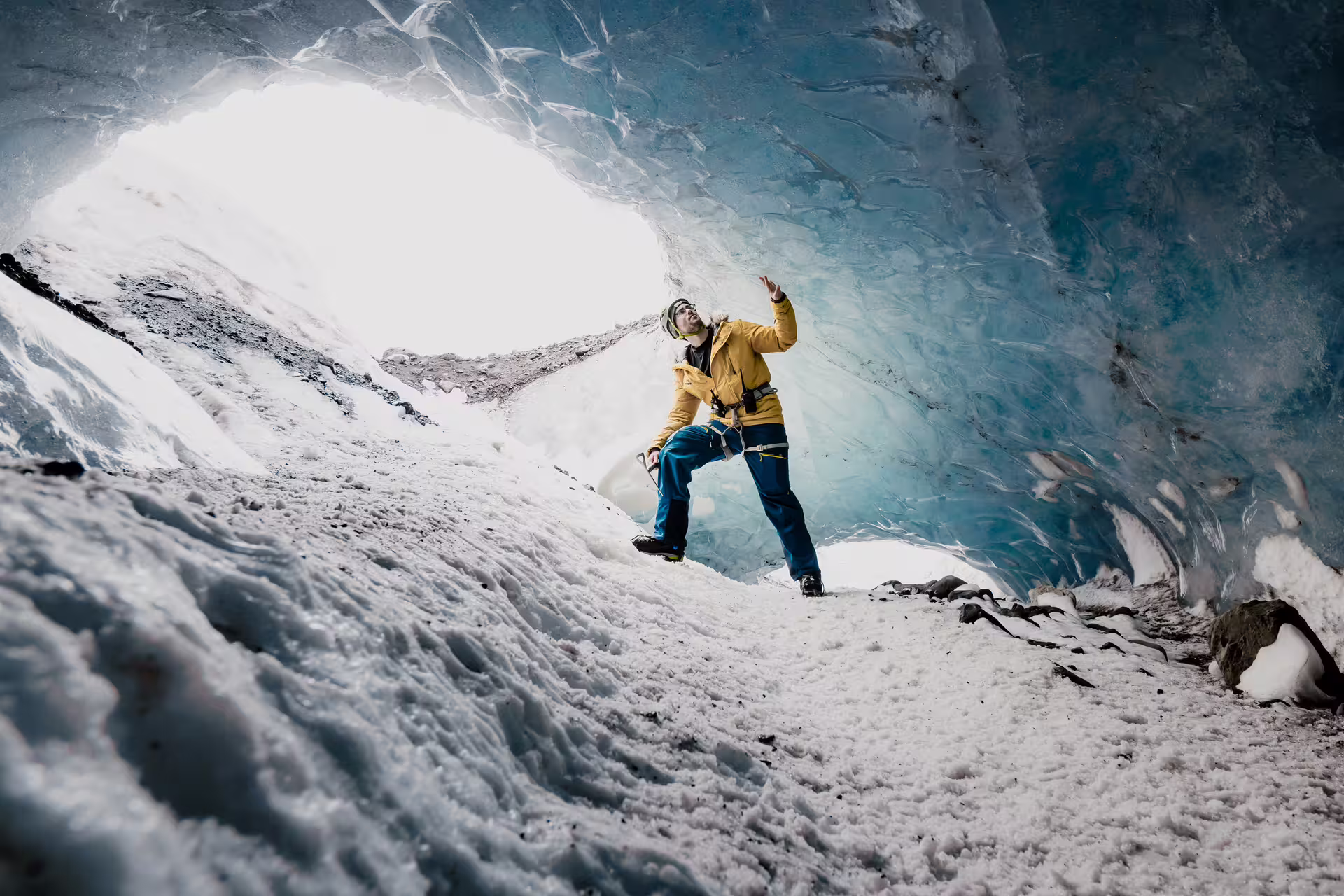 Guide in yellow jacket exploring blue glacial ice cave during Iceland glacier hiking tour