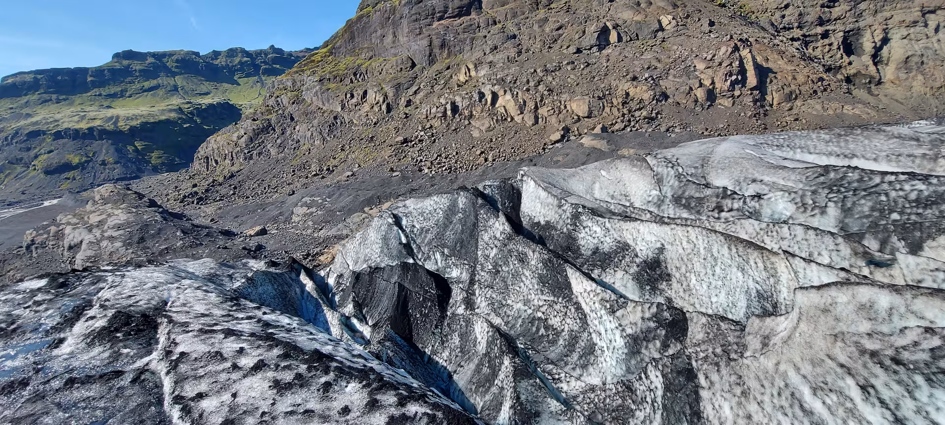 Dark ash-covered glacier ice with deep crevasses and volcanic rocky cliffs in Iceland