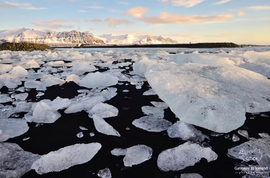 Ice chunks scattered on black sand beach at Jokulsarlon Glacier Lagoon with snowy mountains in Iceland