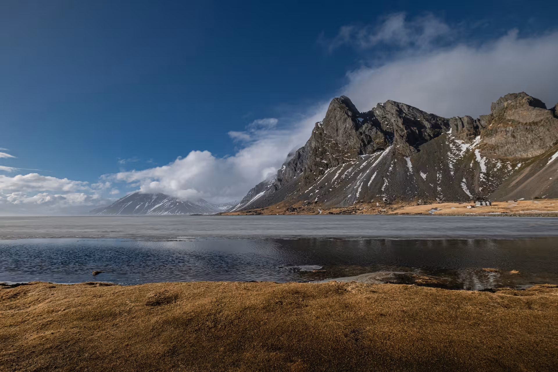 Rocky snow-capped mountains reflecting in a calm glacial lagoon under a blue sky in Iceland