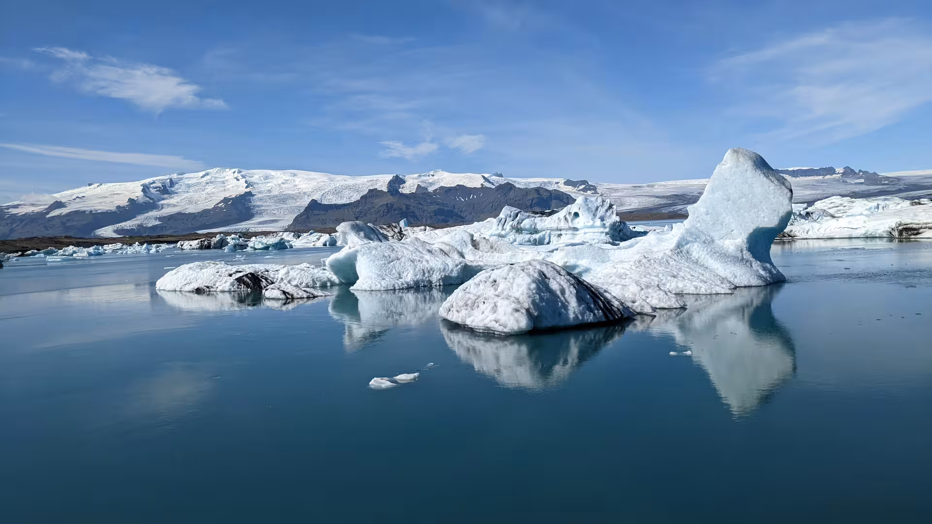 Floating icebergs on the calm blue waters of Jökulsárlón Glacier Lagoon with snow-capped mountains behind