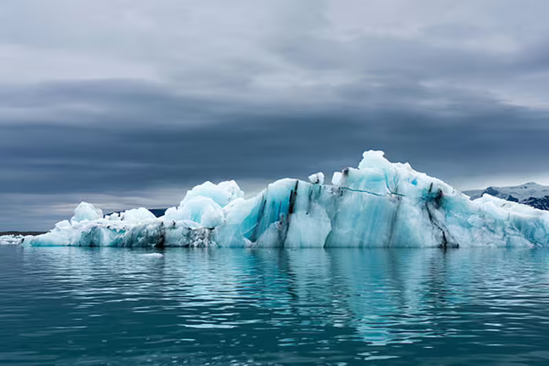 Blue icebergs floating on calm glacial lagoon waters under dramatic cloudy sky in Iceland