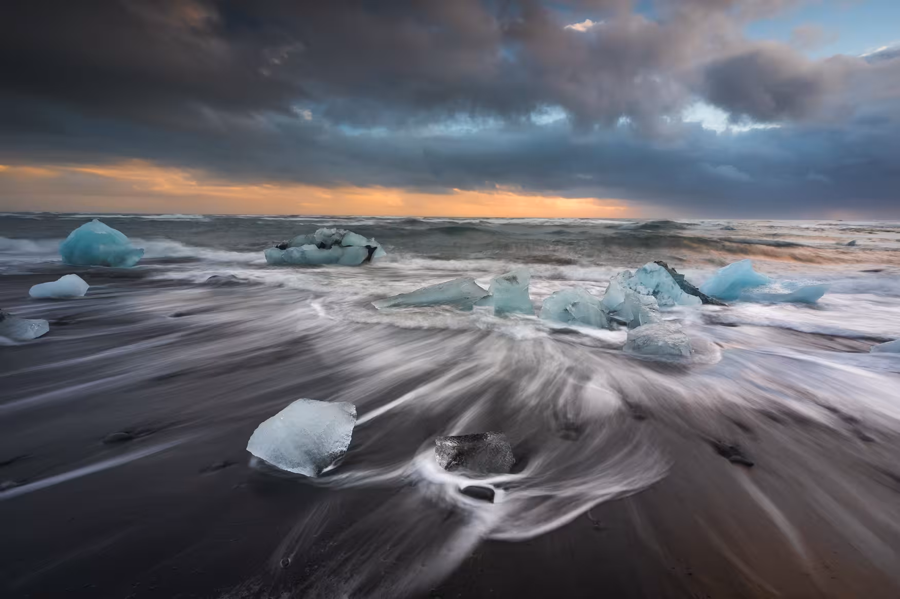 Turquoise ice chunks on black sand beach at Jokulsarlon Glacier Lagoon Iceland during dramatic sunset