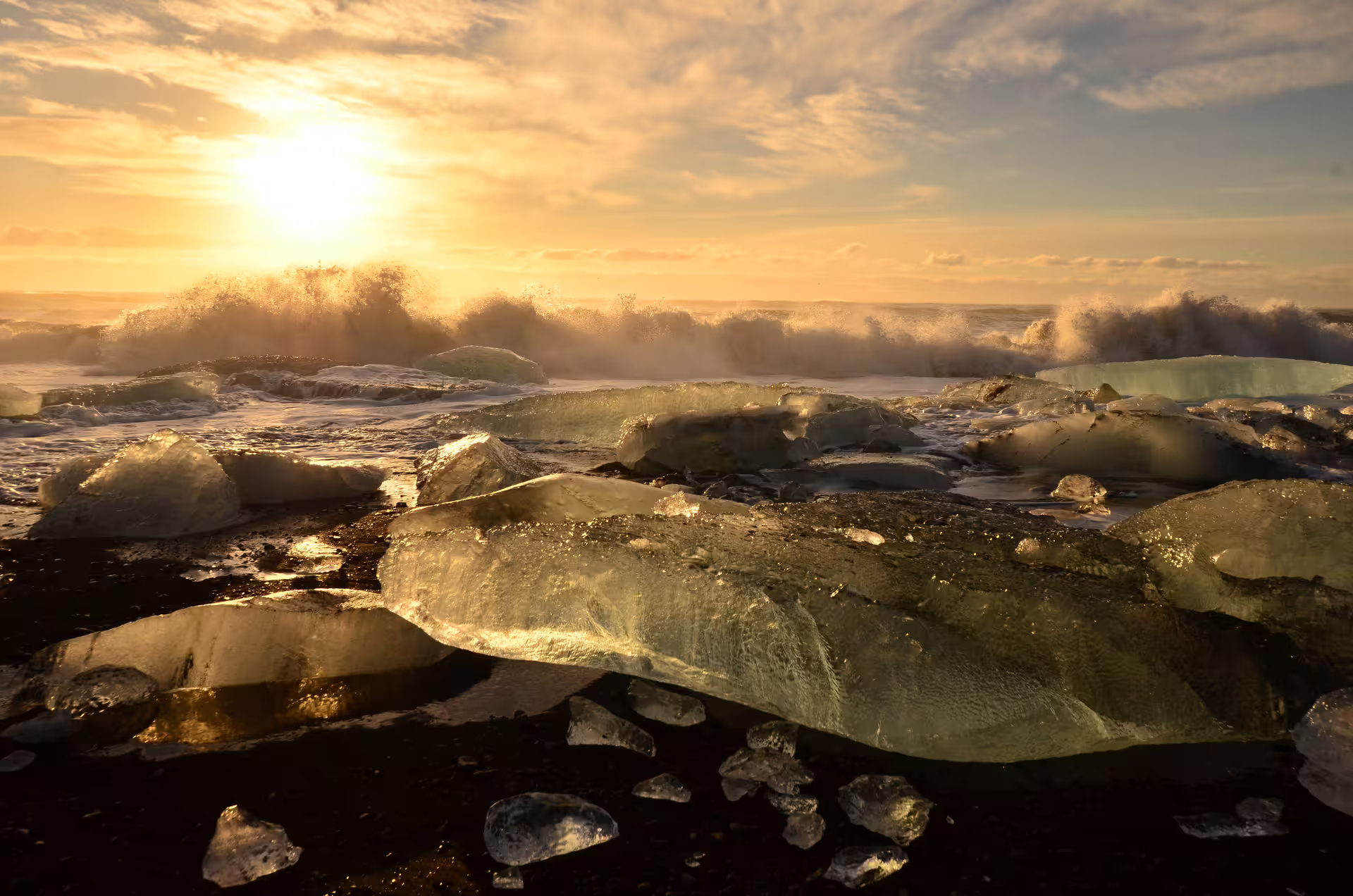 Ice chunks on black sand beach at golden sunset with crashing waves at Iceland's Glacier Lagoon