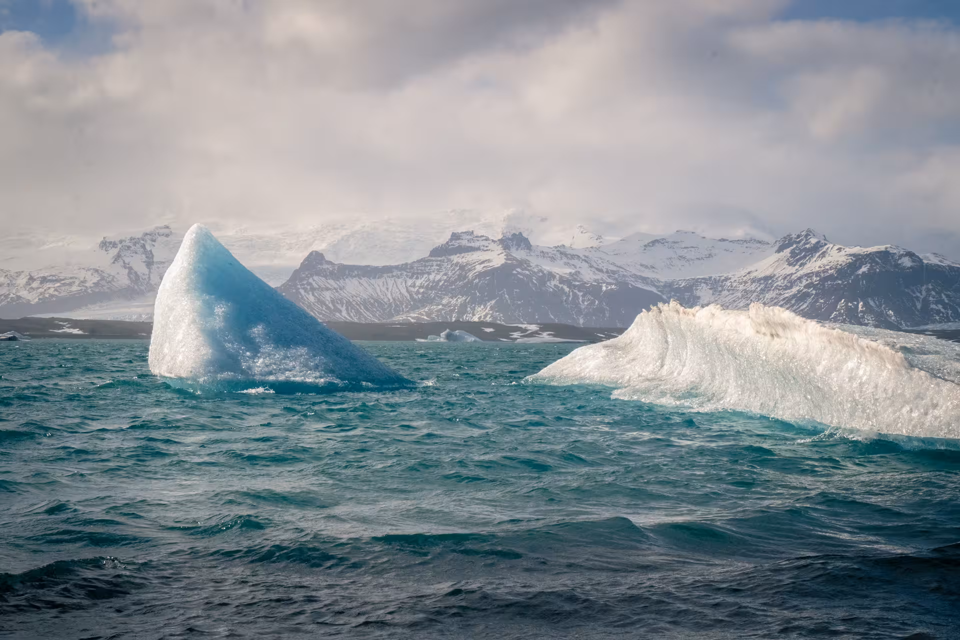 Icebergs floating on turquoise glacial lagoon with snow-capped mountains in background, Iceland