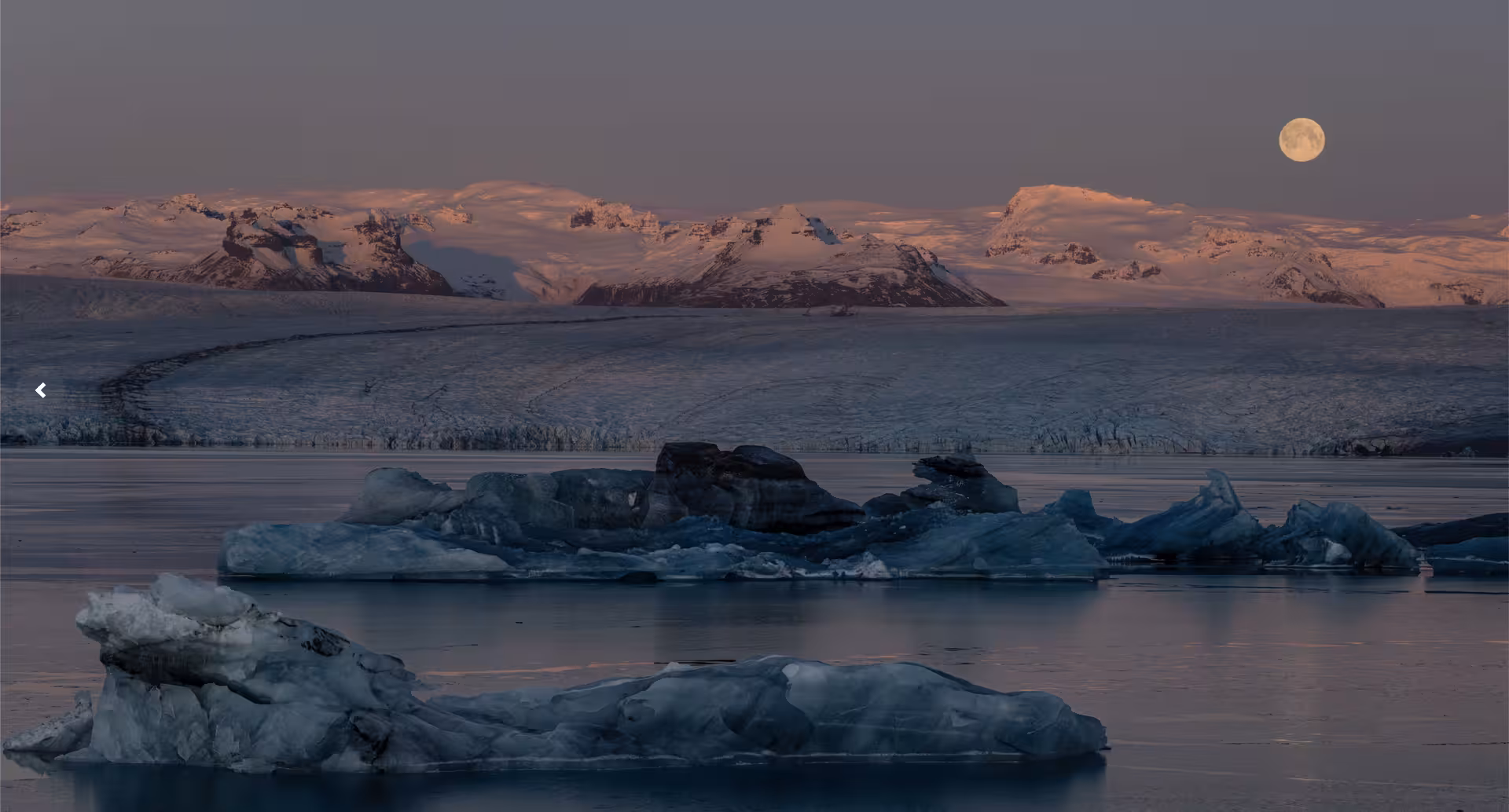Icebergs floating on Jökulsárlón Glacier Lagoon at dusk with snow-capped mountains and full moon, Iceland