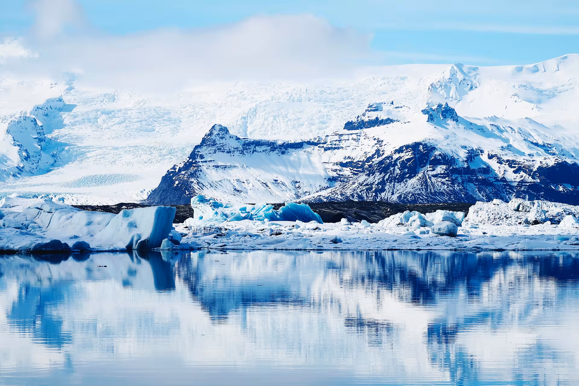 Icebergs floating on Jökulsárlón Glacier Lagoon with snow-capped mountains reflected in calm blue water