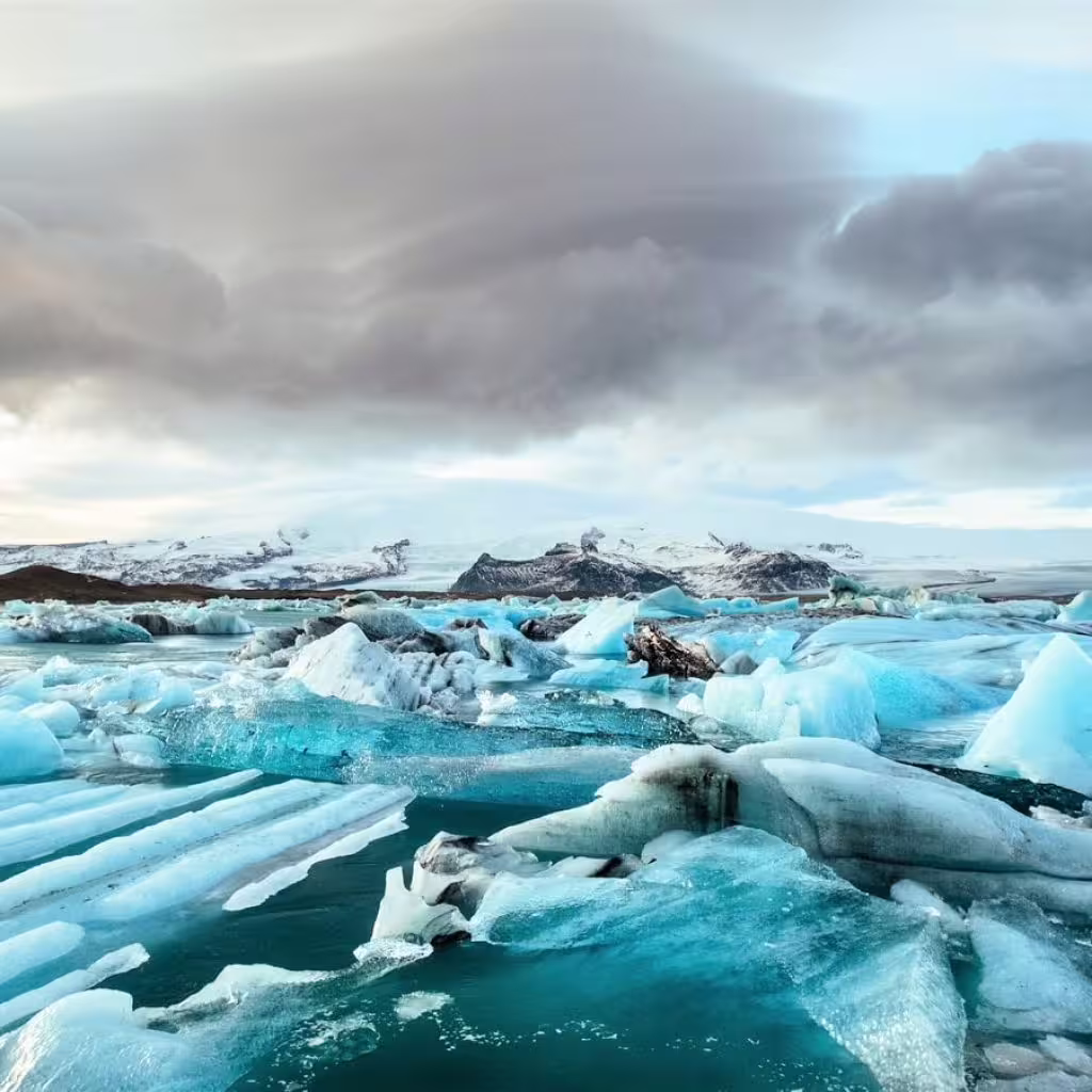 Turquoise icebergs floating in Jökulsárlón Glacier Lagoon with snow-capped mountains and dramatic cloudy sky
