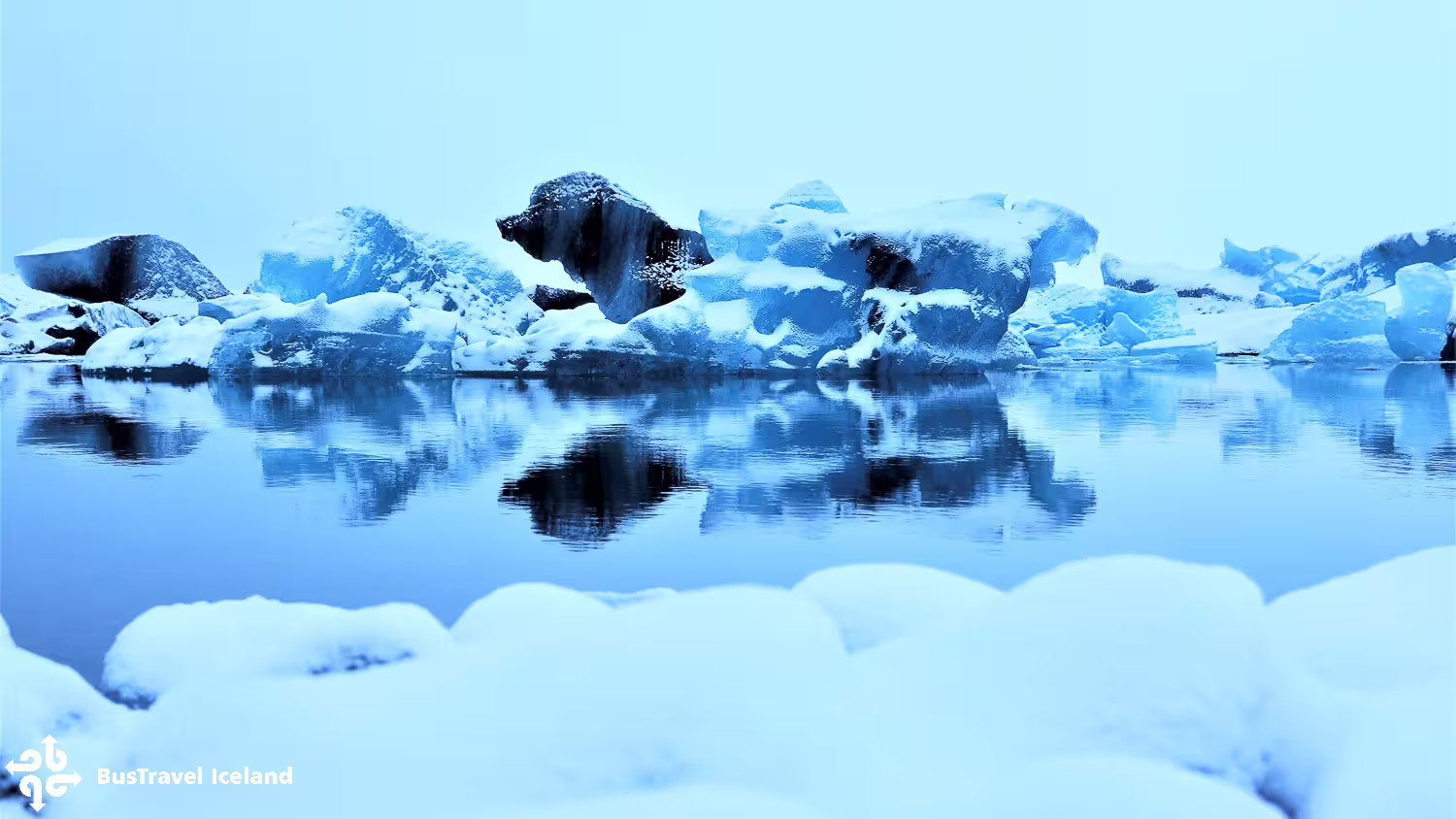 Snow-covered icebergs floating on the calm reflective waters of Jökulsárlón Glacier Lagoon, Iceland