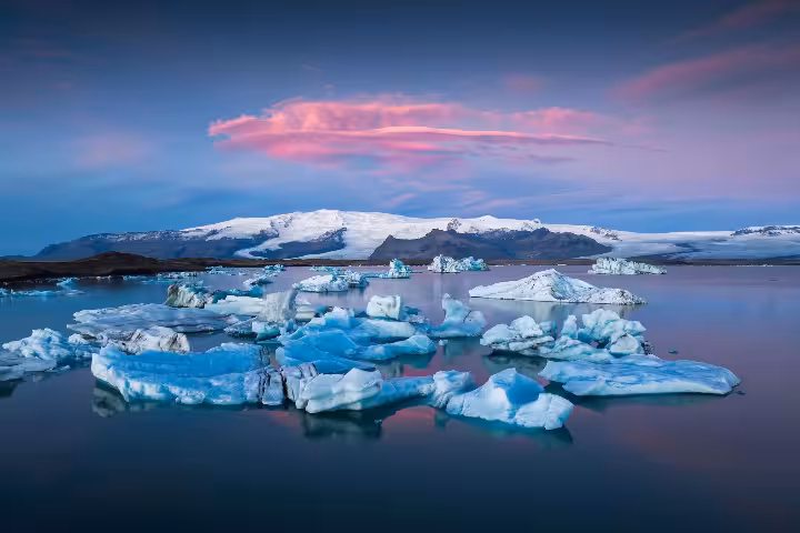 Blue icebergs floating on Glacier Lagoon at sunset with snow-capped mountains in Iceland