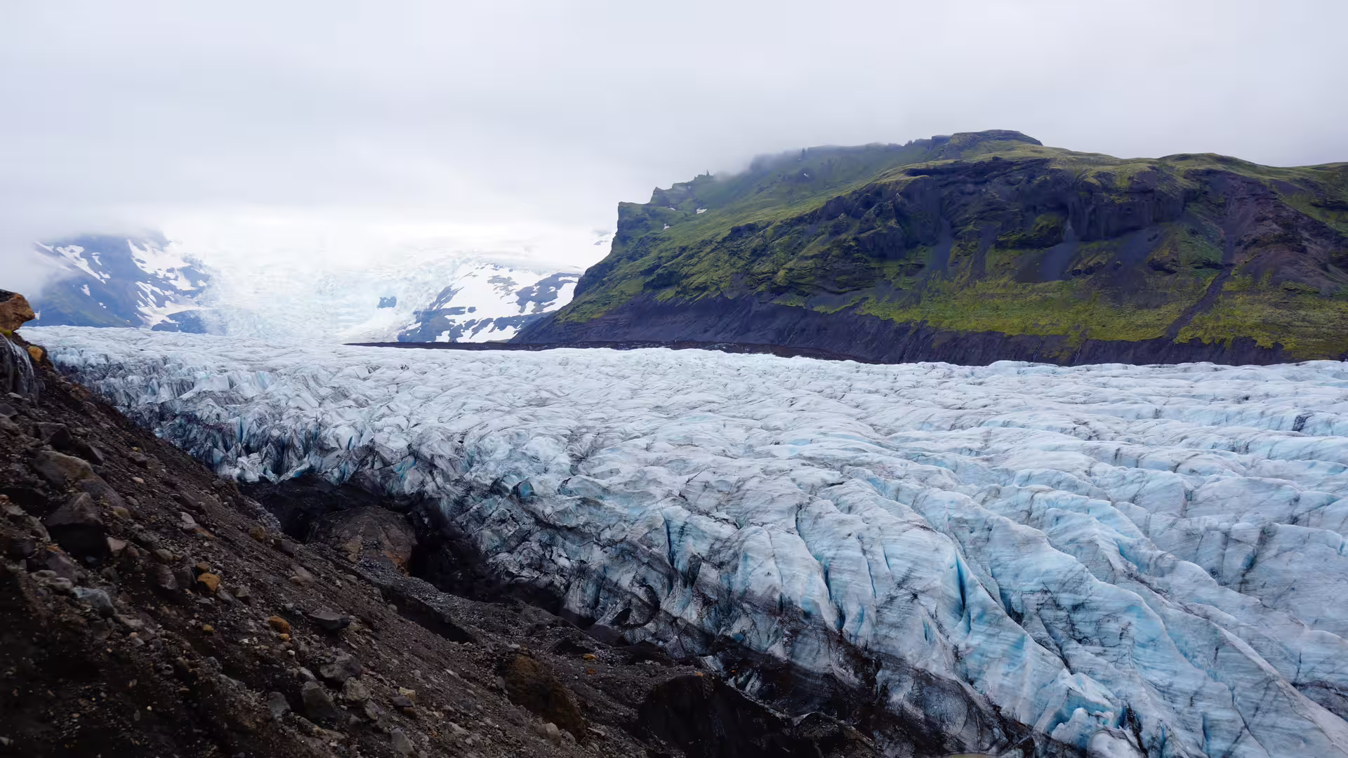Blue glacial ice tongue flowing between dark rocky terrain and green cliffs on Iceland's south coast