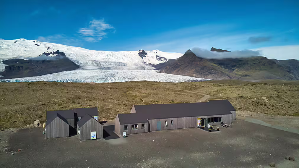 Wooden visitor center building with Skaftafell glacier and snow-capped mountains in background, Iceland