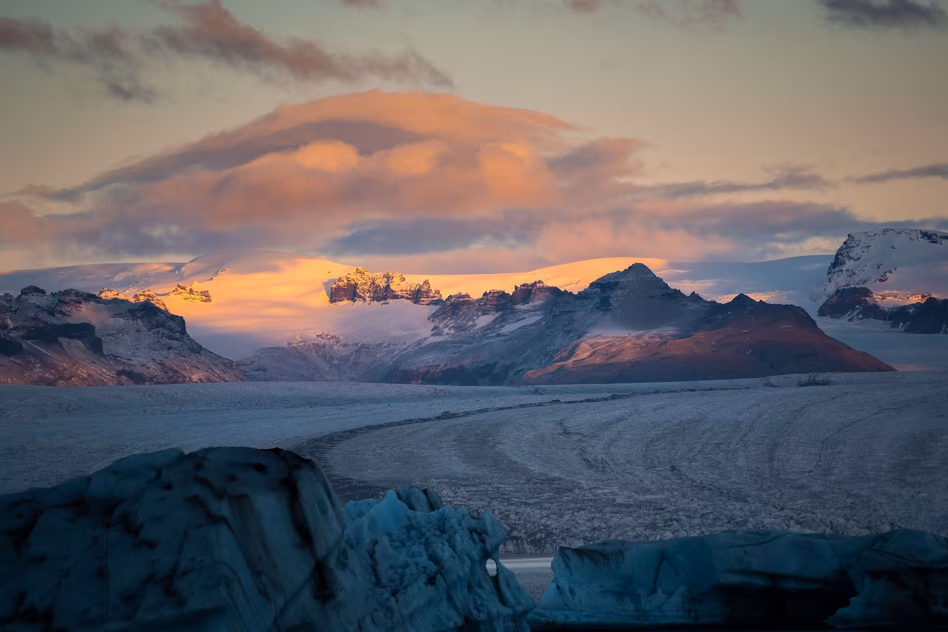 Glacier lagoon and snow-capped mountains bathed in golden sunset light, Iceland
