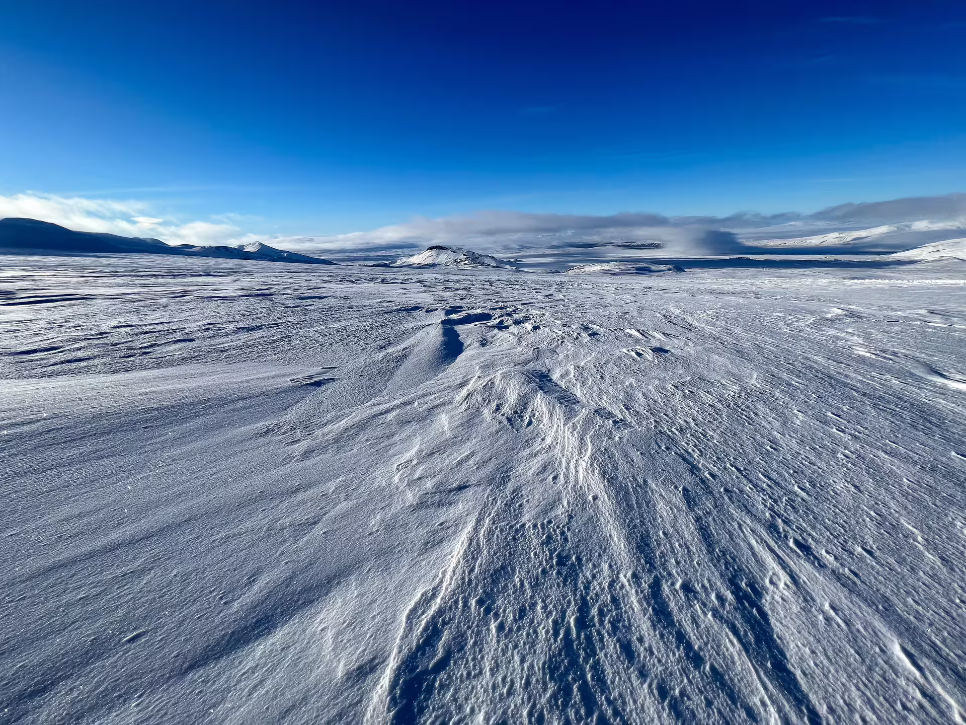 Vast wind-sculpted glacier snowfield with volcanic mountains on the horizon under a clear blue sky