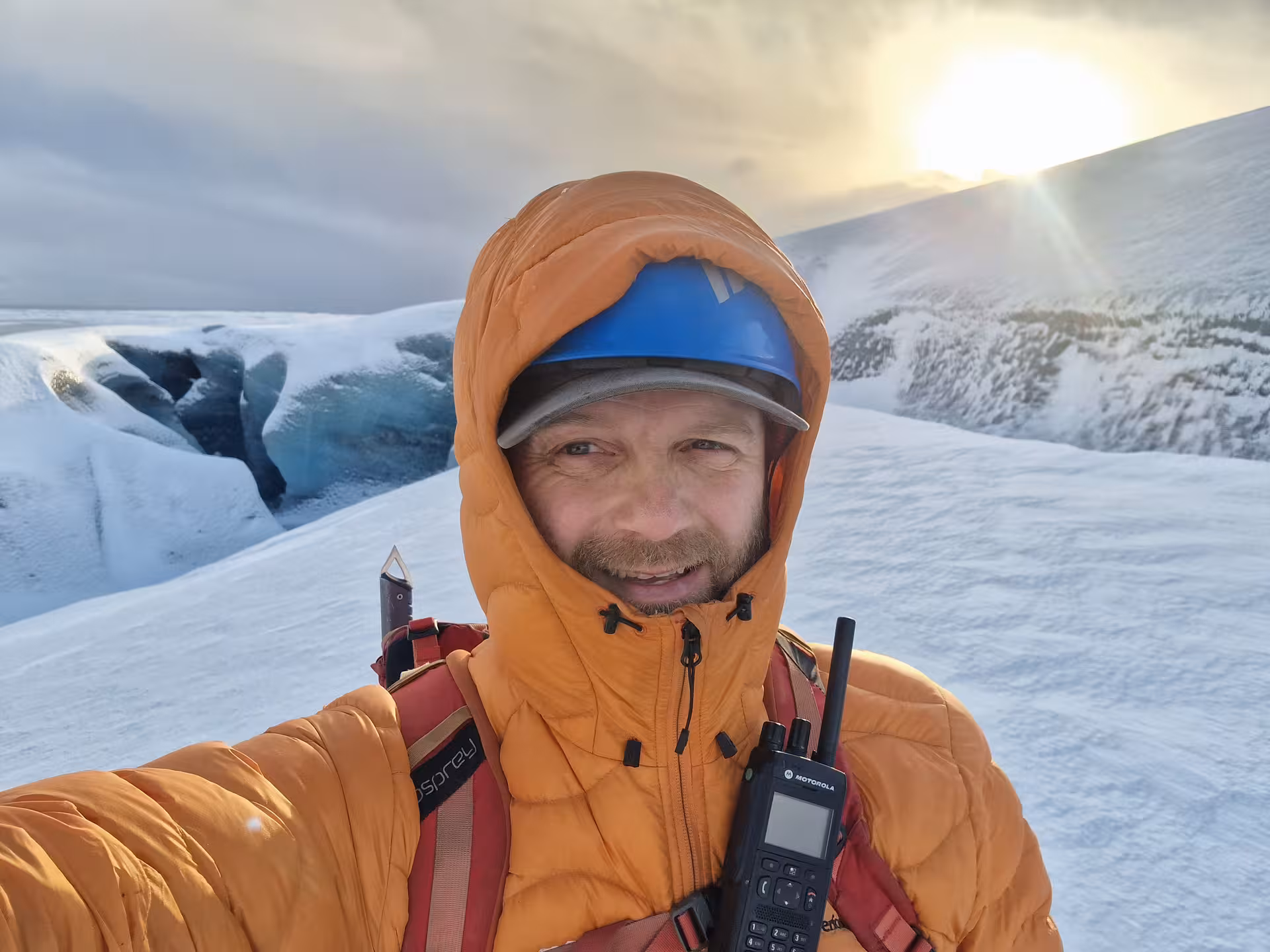 Smiling guide in orange jacket and blue helmet takes selfie on glacier in Southeast Iceland