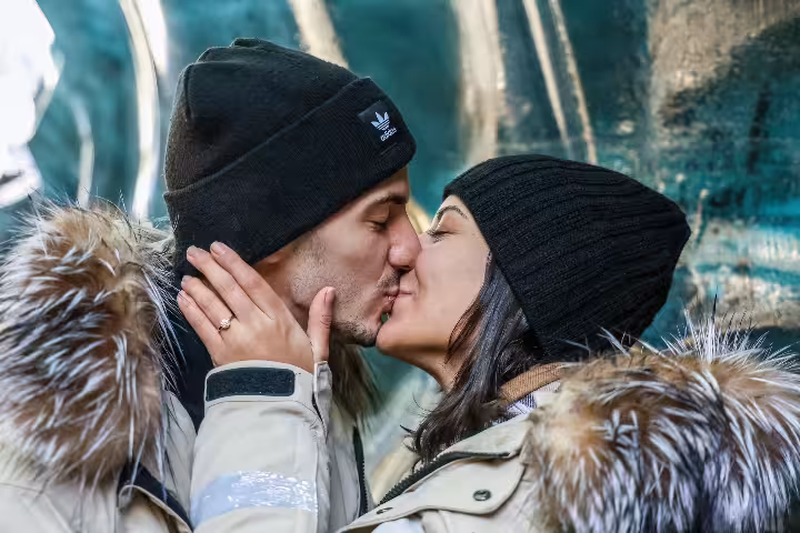Romantic couple sharing a kiss on a glacier adventure proposal tour with an engagement ring visible on her hand