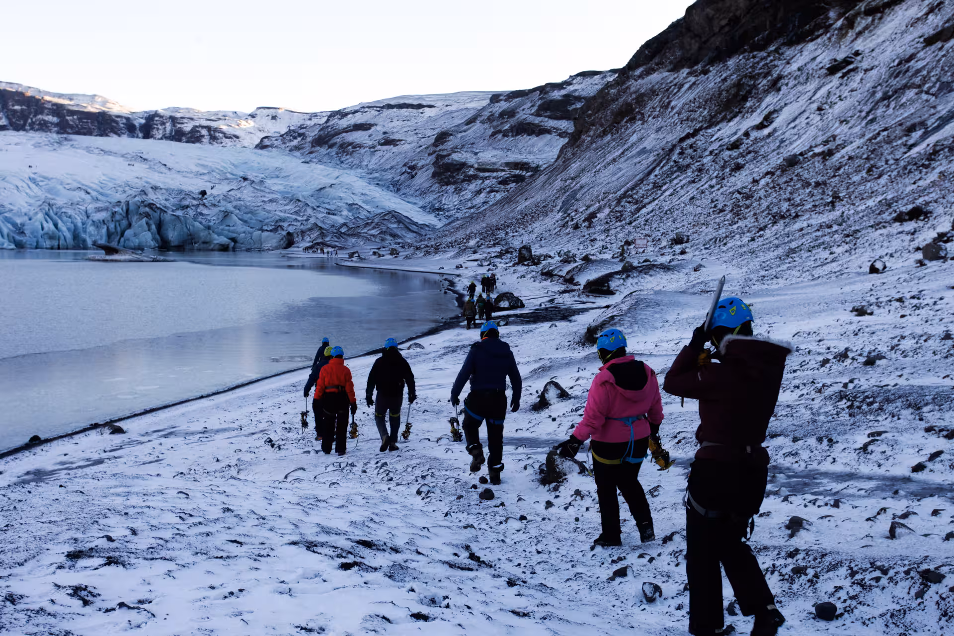 Guided group in blue helmets and crampons walking toward Solheimajokull glacier lagoon in Iceland