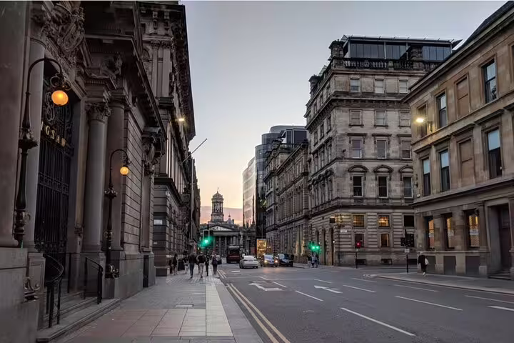 Historic stone buildings lining a quiet Glasgow city street at dusk with green traffic lights