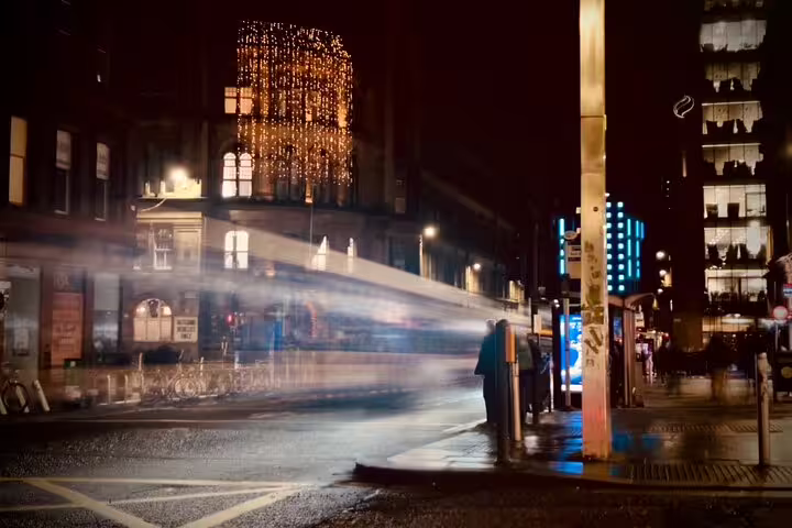 Glasgow city street at night with light trails from passing bus and festive lights on historic building