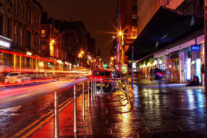 Rainy Glasgow city street at night with glowing lights and motion blur from passing traffic