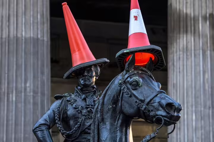 Bronze equestrian statue with orange traffic cones placed on rider and horse heads in Glasgow