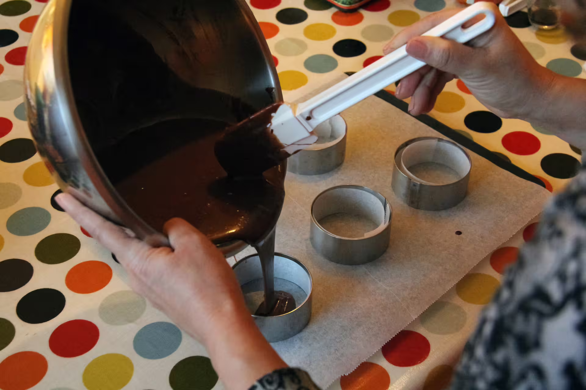 Pouring chocolate batter into round metal cake rings on parchment paper during a Paris cooking class