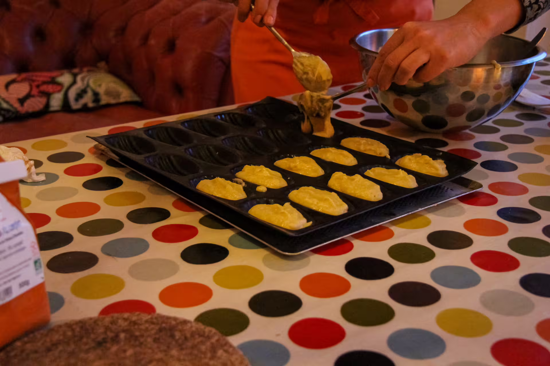 Hands spooning gluten-free madeleine batter into a dark non-stick mold during a Paris cooking class